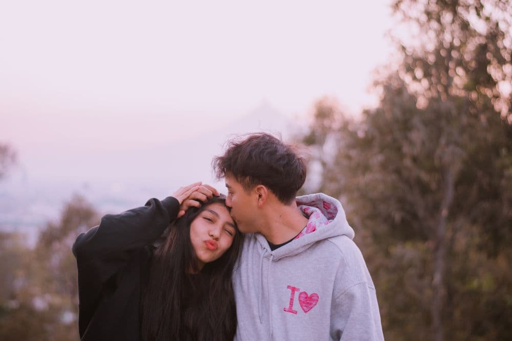 A couple embracing at sunset as one kisses the other's forehead.