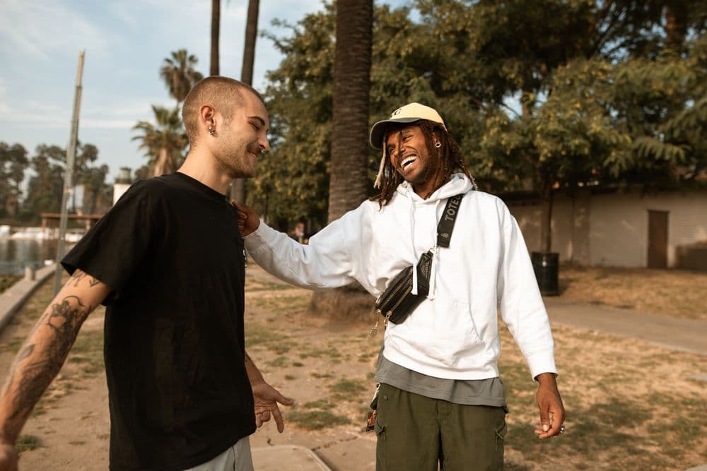 Two friends laughing together on a sunny path beside a lake.