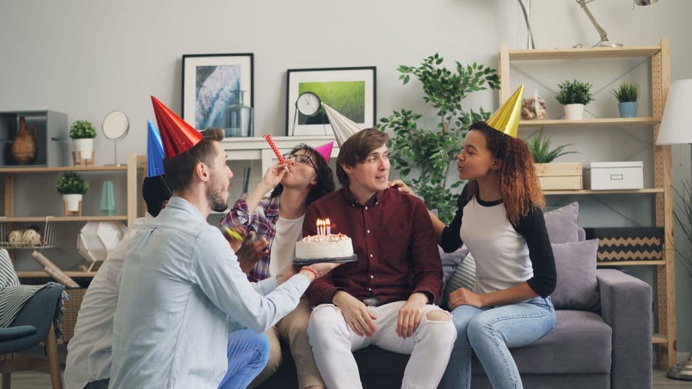 Friends in party hats celebrating with a birthday cake and lit candles.