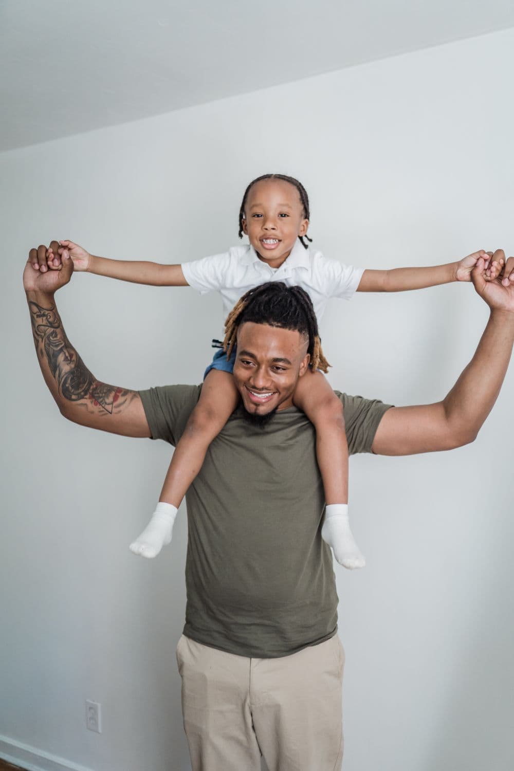 A smiling father carrying his child on his shoulders at home.