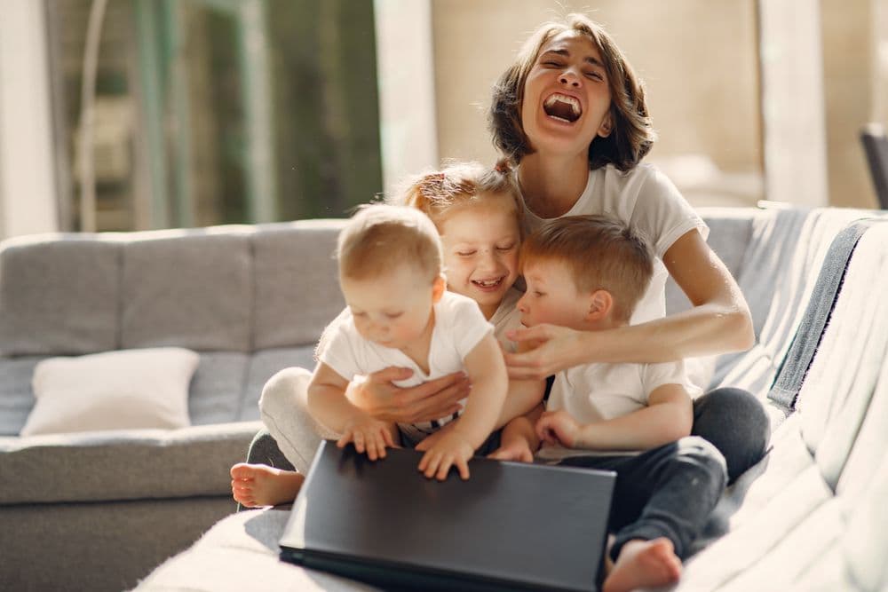 A mother laughing with her three children on a sofa.