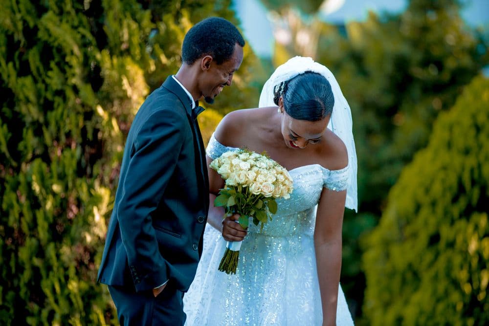A smiling bride and groom with a white bouquet in a green garden.